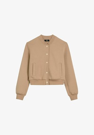 Beżowa krótka kurtka bomber z zapięciem na zatrzaski, prążkowanym kołnierzem, mankietami, pasem oraz dwoma pionowymi kieszeniami z przodu.