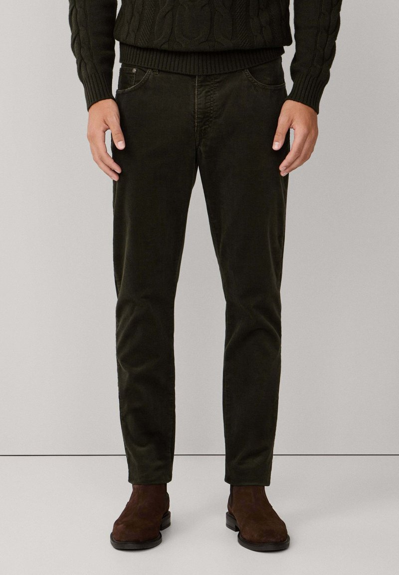 Donkergroene corduroy broek met vijf zakken, slim fit en zichtbare textuur. Bruine suède laarzen complementeren de outfit.