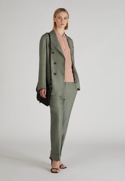 Jasnozielony lniany garnitur z podwójnym zapięciem, w połączeniu z różową bluzką. Charakteryzuje się czarną torebką na ramię i czarnymi sandałami na obcasie.