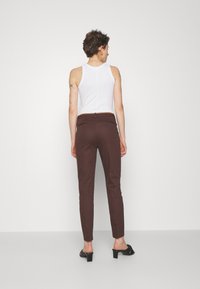 Pantalons marron ajustés avec une texture lisse, comportant des poches arrière et un détail de ceinture marron, associés à un haut sans manches blanc et des sandales à talons noires.