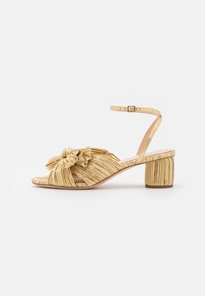 Gyldne hælede sandaler med en struktureret, plisseret design og en fremtrædende sløjfedetail. Ankelslynge med justerbar spænde, mellemstor blokhæl.