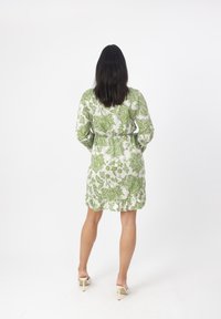 Vestido blanco con patrón floral verde, de mangas largas, con cintura ceñida, dobladillo con volantes y combinado con zapatos de tacón blanco.