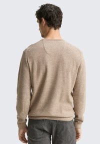 Beige gestrickter Pullover mit strukturiertem Finish, Rundhalsausschnitt und langen Ärmeln, kombiniert mit grauen Jeans, von hinten betrachtet.