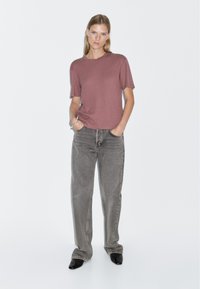 Maroon short-sleeve t-shirt, relaxed fit, paired with high-waisted gray jeans. Model wears black pointed-toe heels, standing against a white background.
