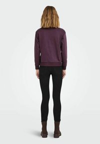 Pullover in cotone di un viola scuro con maniche lunghe, polsini e orlo a coste. Abbinato a leggings neri e stivaletti marroni. Vista dal retro.
