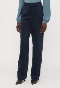 Navy corduroy trousers with a straight-leg fit, featuring a textured surface and a waistband. Paired with pointed toe shoes.
