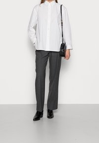 Witte lange mouwen knoopshirt, grijze tailor-made broek en zwarte puntige hakken, met een kleine zwarte crossbody tas.