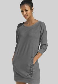 Graues Sweatshirt-Kleid mit langen Ärmeln, Rundhalsausschnitt, seitlichen Taschen und erhabenem "Bench"-Text auf der linken Seite. Glatte Textur.