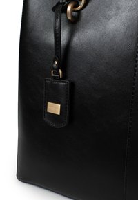 Zwarte leren handtas met een gladde textuur, gouden hardware-accenten en een klein label dat met een lus is bevestigd.