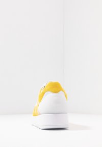 Yellow and white sneaker shown from the back, positioned on a white surface with a plain white background.