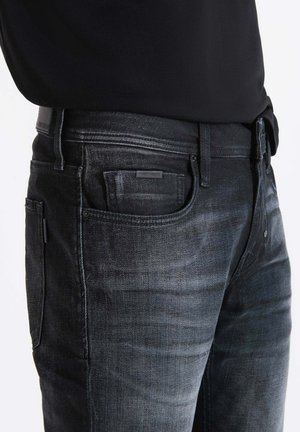 Dark gray denim jeans with a slim fit, visible stitching, front pocket detail, and a leather patch on the waistband. Textured fabric.