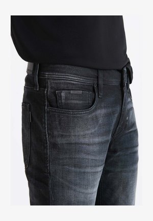 Jeans in denim grigio scuro con vestibilità slim, cuciture visibili, dettagli sulle tasche frontali e una patch in pelle in vita. Tessuto texture.