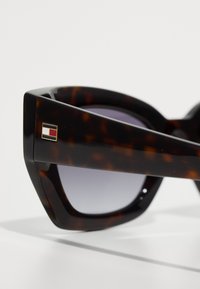 Ochelari de soare din țestoasă cu design geometric, lentile cu degrade și un mic accent metalic în roșu, alb și albastru pe braț.