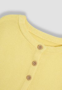 Gul stickad tröja med rund halsringning och tre träknappar. Texturen är mjuk och har ett fint, enhetligt stygnmönster.