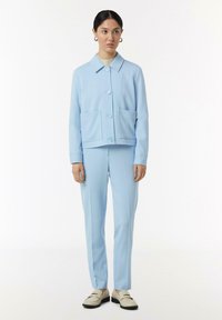 Lichtblauw jasje en broekset gemaakt van een gladde, zachte stof. Het jasje heeft twee voorzakken en een knoopsluiting; slank ontwerp met minimale accenten.