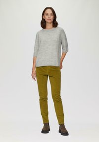 Hellgrauer, gestrickter Pullover mit rundem Ausschnitt und drei Viertelärmeln, kombiniert mit olivgrünen Cordhosen; braune Stiefeletten.