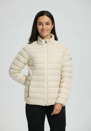 Chaqueta acolchada de color beige claro con diseño de acolchado vertical, cuello alto, cremallera frontal y puños elásticos. Textura suave y hardware minimalista.