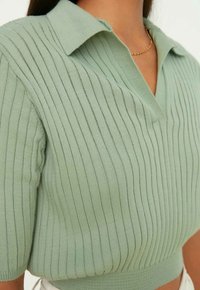 Haut polo tricoté vert menthe avec nervures verticales, manches courtes et col à revers, présentant une coupe décontractée et un tissu texturé.