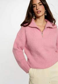 Maglione rosa con zip, caratterizzato da una texture a coste e un ampio colletto. Presenta maniche lunghe e una vestibilità morbida.