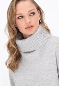 Maglione a collo alto grigio chiaro realizzato in un morbido tessuto testurizzato, caratterizzato da un colletto a costine e una vestibilità comoda.