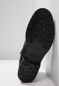 Czarny skórzany but z teksturowaną gumową podeszwą z bieżnikiem. Zamek błyskawiczny z boku, minimalne przeszycia i wytłoczone detale logo.