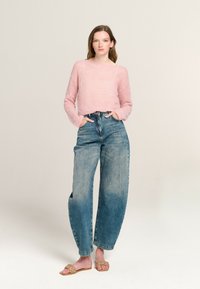 Rosa, strukturiertes Strickoberteil mit quadratischem Ausschnitt; kombiniert mit hochtaillierten, weit geschnittenen, verblassten Jeans aus Denim; flache, gewebte Rutschsandalen.