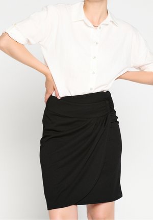 Chemise blanche à manches retroussées associée à une jupe noire mi-longue avec un design drapé et un détail de taille froncée.
