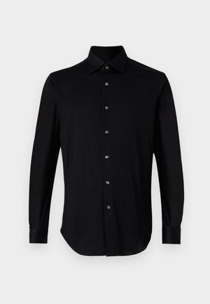 Chemise noire à manches longues en tissu lisse, avec un col pointu, une patte de boutonnage pleine à l'avant et des poignets boutonnés.