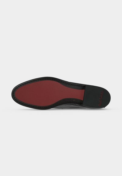 Semelle d'une chaussure habillée en cuir noir avec semelle rouge et talon noir, montrant la signature embossée sur le talon.