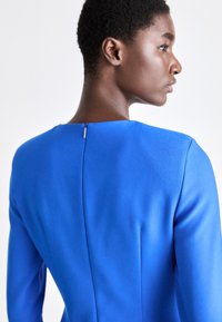 Δομημένο φόρεμα από ζωντανό μπλε ύφασμα με λεία υφή. Διαθέτει στρογγυλή λαιμόκοψη και διακριτική λεπτομέρεια με φερμουάρ στο πίσω μέρος.