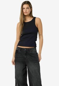 Top negro de canalé combinado con pantalones vaqueros de mezclilla negros sueltos. La parte superior tiene un escote redondo y un diseño sin mangas. Los jeans cuentan con bolsillos frontales.