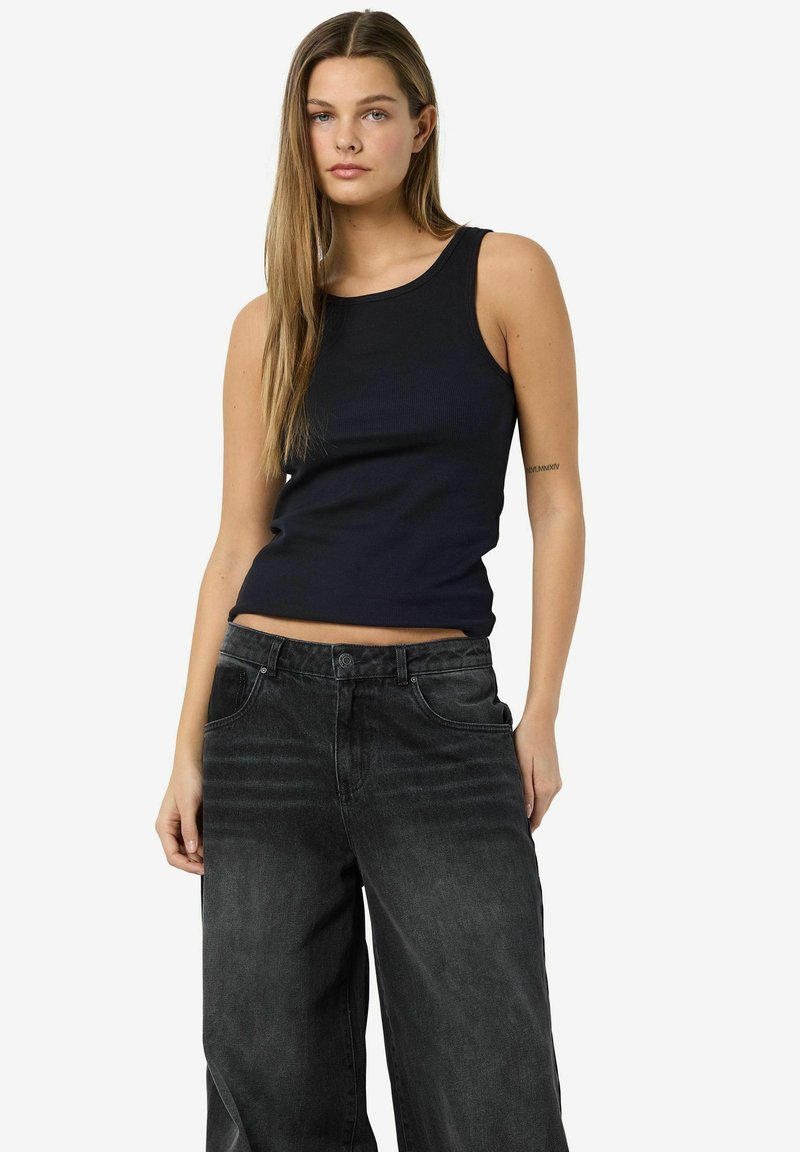 Top negro de canalé combinado con pantalones vaqueros de mezclilla negros sueltos. La parte superior tiene un escote redondo y un diseño sin mangas. Los jeans cuentan con bolsillos frontales.