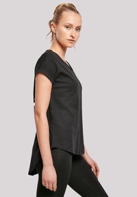 Black short-sleeve top with a V-neck, relaxed fit, and longer back hem. Made from soft, lightweight fabric, featuring subtle stitching details.