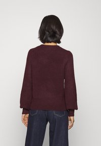 Viininpunainen neulepaita, jossa on teksturoitu pinta, resorilla viimeistelty pääntie ja helma sekä hieman puffitetut hihat. Yhdistetty tummiin denimhousuihin.