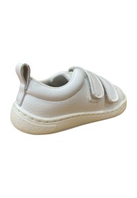 Zapato blanco de cuero con un acabado texturizado, correas de velcro y suela de goma. Presenta un pequeño tirador en el talón y acentos cosidos.