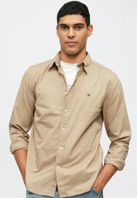 Camicia beige con bottoni, maniche lunghe, colletto e un piccolo logo sul petto. Realizzata in tessuto morbido, presenta una vestibilità classica.