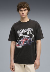 Tricou oversized negru cu decolteu la baza gâtului, având un grafic cu o mașină de curse roșie și textul "SCUDERIA FERRARI" pe față.