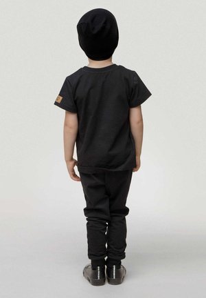 Schwarzes Kinderoutfit bestehend aus einem T-Shirt mit kurzen Ärmeln und schmal zulaufenden Hosen, beide in einer einheitlichen Farbe, ergänzt durch eine schwarze Mütze.