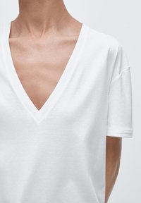 Witte korte mouw t-shirt met een diepe V-hals. Gemaakt van zachte stof met een gladde textuur en minimale stiksel-details.