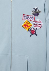 Felpa con cappuccio azzurro chiaro con zip e cinque patch ricamati a tema baseball sul petto, tra cui una silhouette di giocatore, una mazza, una palla e dettagli testuali.