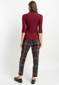 Bordowy golf o dopasowanym kroju, w zestawieniu z szarymi spodniami w kratkę z pomarańczowymi akcentami. Gładka struktura i długość do połowy łydki.