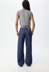 Šedý top bez rukávů v kombinaci s širokými tmavomodrými džíny. Džíny mají nášivku na pásku a dvě zadní kapsy. Hladká textura.