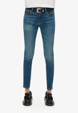 Jeans de mezclilla azul ajustados con un lavado desvaído, que cuentan con bolsillos delanteros, un cinturón negro con hebilla metálica y mocasines negros.