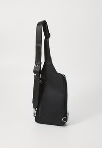 Bolso cruzado de tela negra con correa ajustable, compartimento principal con cremallera y acentos de hardware en plata. Diseño simple y funcional.