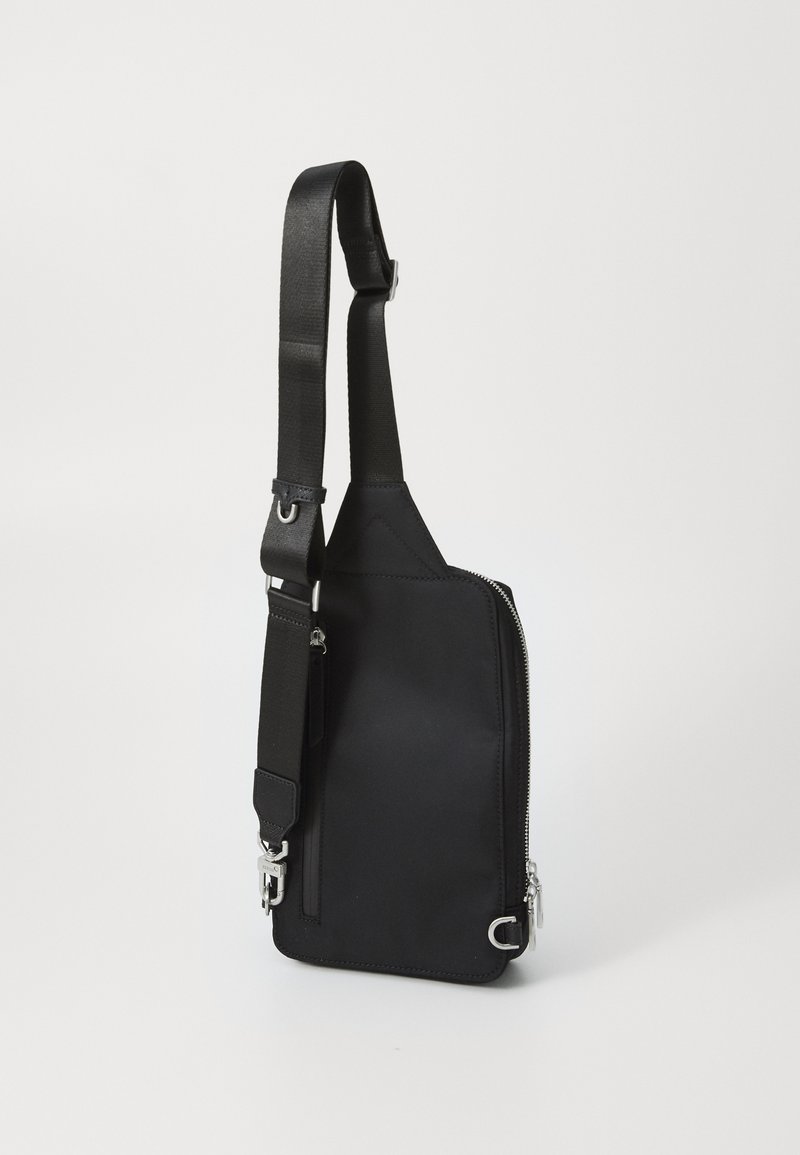 Bolso cruzado de tela negra con correa ajustable, compartimento principal con cremallera y acentos de hardware en plata. Diseño simple y funcional.