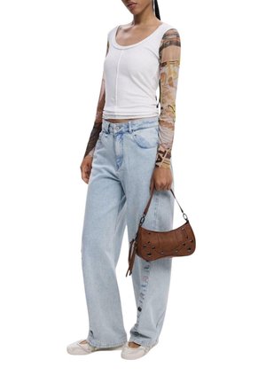 Top bianco aderente con maniche lunghe trasparenti e decorate, jeans azzurri a vita alta e borsa marrone con dettagli decorativi. Scarpe bianche.
