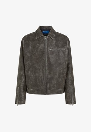 Pelēka ādas jaka ar rāvējslēdzēju priekšā, sīku apkakli un kabatu kreisajā krūtī. Ar rāvējslēdzējiem uz piedurknēm un teksturētu virsmas apdari.