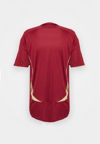 Czerwona koszulka sportowa z krótkim rękawem, z złotymi akcentami po bokach. Gładki materiał z pionowym prążkowanym wzorem.