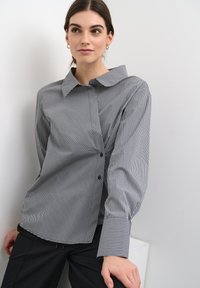 Black and white striped button-up shirt with a collar, long sleeves, and contrasting cuffs. Fabric has a smooth texture.