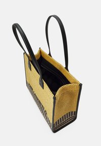 Tkaná slaměná taška s černými koženými uchy. Má strukturované žluté tělo a vzorovaný černý pruh na dole. Vnitřek je černý.